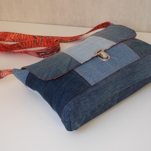 Peut inclure: Sac bandoulière en patchwork de denim avec fermeture à fermoir argenté. Le sac est doté d'une bandoulière à motifs rouges et oranges. Fabriqué à partir de différents tons de denim bleu.
