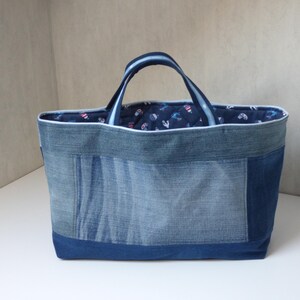 Op de afbeelding: Een blauwe denim tote bag met een witte rand en een blauwe en witte bedrukte voering. De tas is gemaakt van gerecycled denim en heeft een patchwork ontwerp.