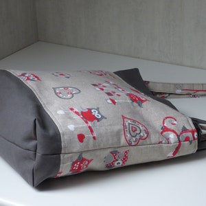 Peut inclure: Un sac cabas gris et beige avec un imprimé hibou rouge et blanc. Le sac est doublé de tissu gris et possède une longue bandoulière grise.