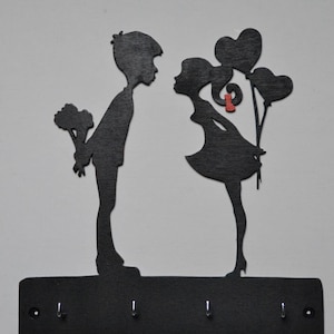 May include: Black silhouette key holder featuring a couple holding flowers and balloons. The couple stands on a black base with four hooks.