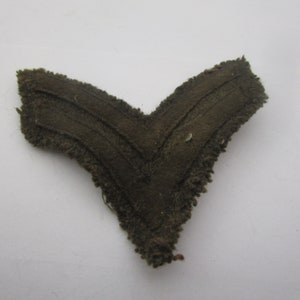 May include: A brown fabric chevron patch with two stripes. The patch is frayed around the edges.