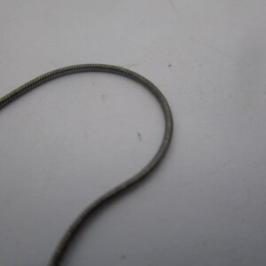 以下が含まれることがあります： テクスチャ加工された表面を持つシルバーチェーンネックレスのクローズアップ。