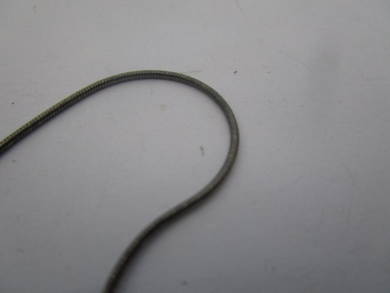 以下が含まれることがあります： テクスチャ加工された表面を持つシルバーチェーンネックレスのクローズアップ。