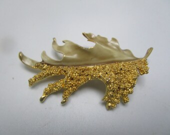 May include: A gold-toned leaf-shaped brooch with a textured design. The leaf is smooth on top and has a textured, bumpy underside.