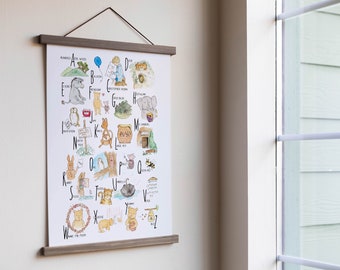 Può includere: Un poster dell'alfabeto a tema Winnie the Pooh con illustrazioni di personaggi del libro. Il poster è incorniciato con una cornice di legno ed è appeso a una parete bianca.