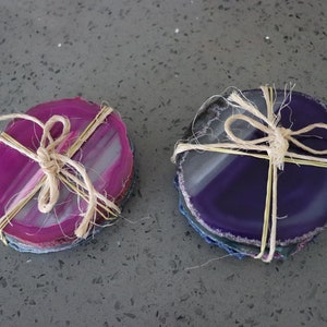 May include: Two sets of agate coasters, one set is pink and white, the other is purple and white. Both sets are tied together with twine.