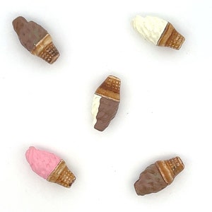 May include: Five miniature ice cream cones in various colors and flavors. The cones are made of brown, white, and pink. The ice cream is chocolate, vanilla, and strawberry.