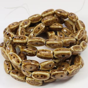 May include: A strand of brown and white ceramic beads with a speckled pattern. The beads are oval shaped and have a glossy finish.