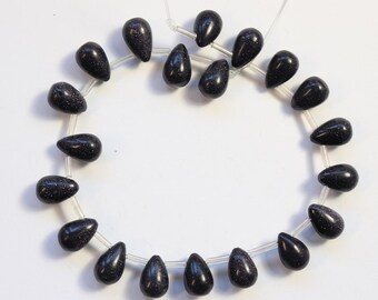 May include: A strand of black gemstone beads in a teardrop shape. The beads are strung on a clear elastic cord.
