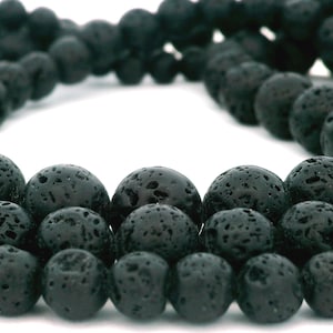 May include: Close-up of strands of black lava rock beads. The beads are round and have a porous texture. The beads are strung together, creating a necklace or bracelet. The background is white.