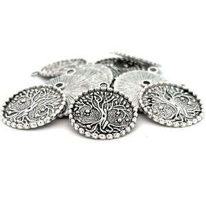 May include: A pile of silver-toned metal charms featuring a tree of life design. The charms have a beaded edge and a hole for attaching to jewelry.
