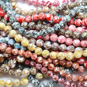 May include: A close-up of a collection of colorful beads in various shades of red, pink, yellow, gray, and brown. The beads have a marbled appearance and are strung together, suggesting they are for jewelry making or crafts.