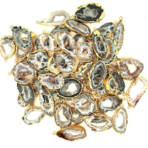May include: A collection of agate slices with gold-plated edges. The slices are various shades of gray, white, and black, and have a natural, organic shape. Each slice has a hole drilled through it, making them suitable for jewelry making or other crafting projects.