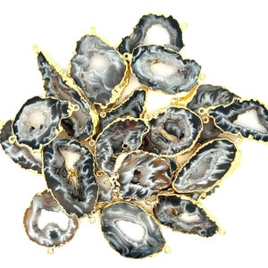 May include: A collection of agate slices with gold-plated edges. The natural stone features a mix of gray, white, and brown patterns. Each slice has a unique shape and a small loop for hanging.