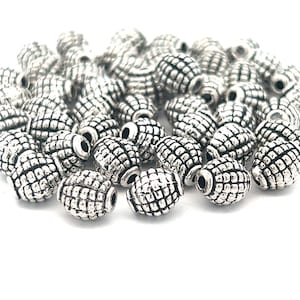 May include: A pile of silver oval-shaped beads with a textured surface. The beads have a hole in the center for stringing.