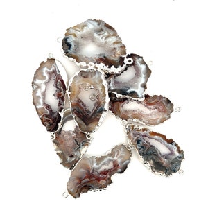 May include: A group of seven agate slices with silver-toned metal accents. The agate slices are brown, white, and gray with a natural crystal pattern. The slices are arranged in a cluster, with some overlapping.