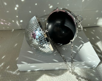 May include: A silver disco ball-shaped clutch purse with a chain strap. The purse is open, revealing a black interior.