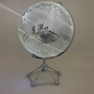 Puede incluir: Un globo terráqueo de discoteca plateado en un trípode. La bola está hecha de muchas pequeñas baldosas espejadas.