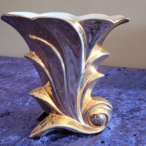 May include: A vintage art deco vase with a striking design. The vase features a metallic purple body with gold accents and a white scalloped rim. The gold detailing highlights the vase's curves and adds a touch of elegance. A decorative piece for any home.