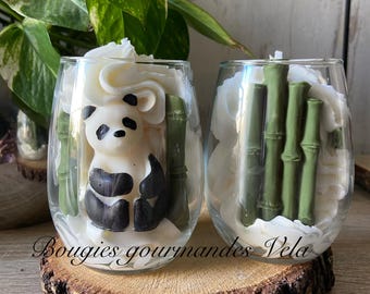 May include: Two clear glass candle holders on a wooden slice. One candle features a panda bear design with black and white details and green bamboo. The other candle has green bamboo. The text "Bougies gourmandes Vela" is visible.