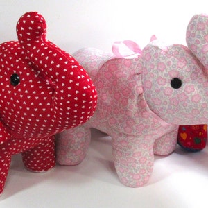 May include: Handmade fabric elephant toys in red with white hearts, pink floral, and red with colorful hearts patterns. Each elephant has a black button eye and a ribbon tied around its ear. These plush toys are suitable for children.