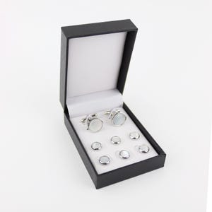 May include: A black box with a white interior containing a set of silver cufflinks and shirt studs. The cufflinks and studs have a white mother-of-pearl inlay.