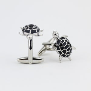 May include: Two silver cufflinks with a black turtle design. The turtles have a detailed shell pattern and are set against a white background. The cufflinks are designed for formal wear.