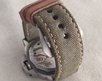 May include: A close-up of a watch with a green canvas strap and a brown leather accent. The watch face is visible and says "Officine Panerai".
