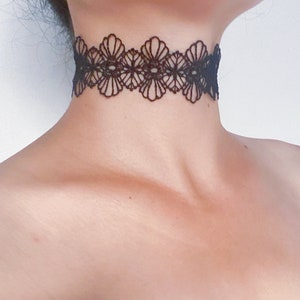 May include: Black lace choker necklace with a floral design. The choker is made of delicate, openwork lace and sits around the neck. The intricate pattern is visible against the skin.