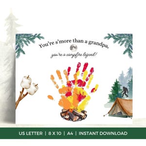 Puede incluir: Tarjeta blanca con el texto "You're s'more than a grandpa, you're a campfire legend!" con un diseño de huella de mano en rojo, amarillo y naranja, que se asemeja a una fogata. Ilustraciones de malvaviscos, árboles y una tienda de campaña.
