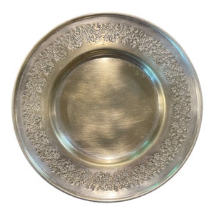 May include: A silver plate with a floral design around the edge. The plate is round and has a smooth, shiny surface.
