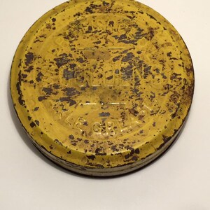 Puede incluir: Tapa de metal amarilla con las palabras "W.M. BULLENS AXLE GREASE" impresas en ella. La tapa est&aacute; oxidada y desgastada.