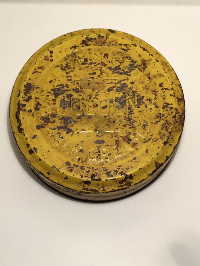 Puede incluir: Tapa de metal amarilla con las palabras "W.M. BULLENS AXLE GREASE" impresas en ella. La tapa est&aacute; oxidada y desgastada.