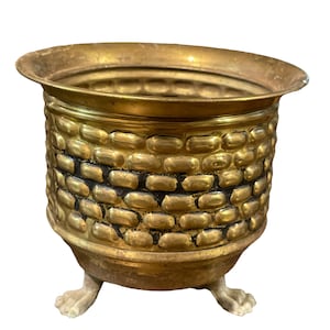 May include: A gold metal planter with a textured design and three white feet.
