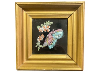 May include: A framed artwork featuring a butterfly with pink and blue wings, surrounded by white flowers on a black background.