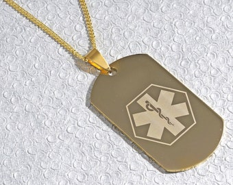 May include: Gold chain necklace with a gold dog tag pendant featuring a medical symbol engraved on the front. The symbol is a six-pointed star with a snake wrapped around it.