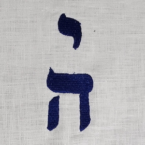 Pode incluir: Um tecido branco com a palavra hebraica "Chai" bordada em fio azul.