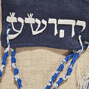 May include: A blue fabric bag with white embroidered Hebrew text "קדוש" and blue and white braided tassels.