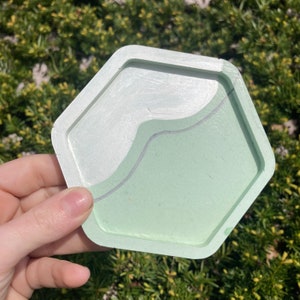 May include: A hexagonal coaster with a light green and white marbled design. The coaster has a raised edge and a smooth finish.