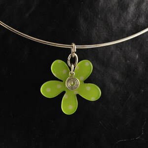 May include: A silver necklace with a green flower pendant. The flower has white polka dots and a silver swirl in the center.
