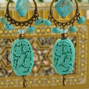 Peut inclure: Boucles d'oreilles turquoise bleu avec un motif d'oiseau sculpté, une pierre turquoise et un anneau en laiton. Les boucles d'oreilles sont suspendues à un support en laiton.