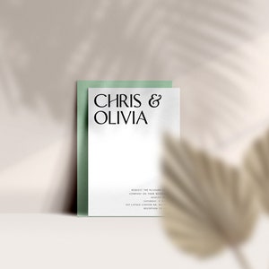 May include: A wedding invitation featuring the names "Chris & Olivia" in elegant black font. The invitation is on a white background, set against a pale green backing. The design includes additional text and is set against a neutral background with a shadow.