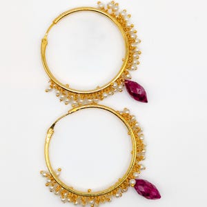 May include: A pair of gold hoop earrings with a dangling pink gemstone and white pearl accents.