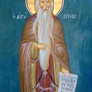 May include: A religious icon painting of a bearded man with a halo, holding a scroll with Greek text. The text on the scroll reads "ETIN ON AVTOIC TO FWS ANATAV CIC BPO CICACIC XAPA". The background is a teal blue color.