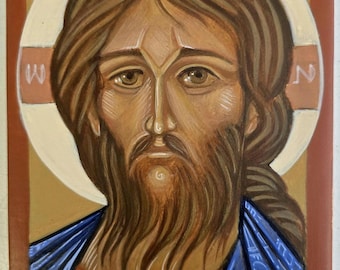 May include: A rectangular religious icon painting featuring a portrait of a bearded figure with long brown hair. The figure wears a blue garment over a reddish-brown tunic. A white halo with a cross symbol is behind the head, with Greek letters.