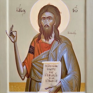 Puede incluir: Icono que representa una figura con cabello largo castaño y barba, vestida con una túnica roja y azul. La figura sostiene un pergamino con texto y tiene un halo dorado. El fondo es de color beige claro.