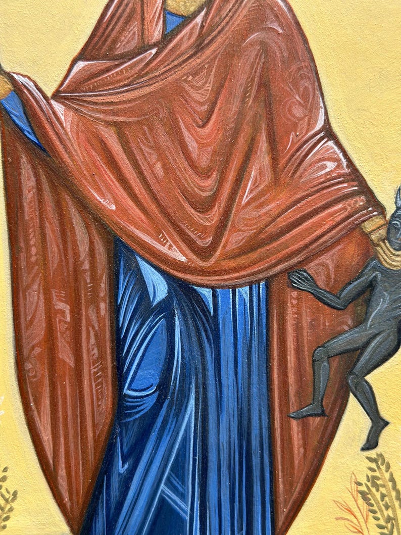 May include: A close-up of a religious icon painting depicting a figure wearing a red robe and blue dress. A small black figure is depicted at the bottom right of the image.