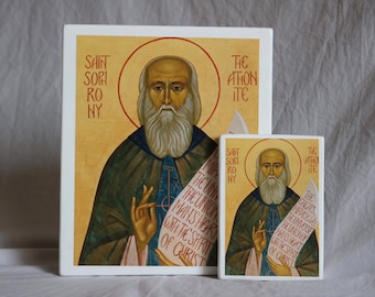 May include: A white ceramic tile with a painted icon of Saint Sophrony of Essex. The icon depicts a bearded man in a brown robe holding a scroll with the text "The union of the union man's heart with the spirit of Christ". The tile is framed with a white border.
