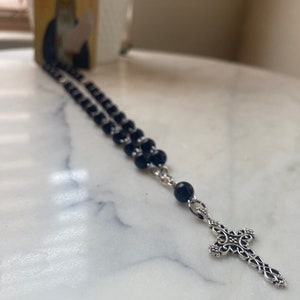 May include: A black beaded rosary with a silver cross pendant. The beads are round and the cross has a detailed design.