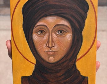 May include: A rectangular wooden icon painting featuring a portrait of Saint Theodosia of Constantinople. The figure wears a dark brown head covering against a vibrant yellow background with a red halo. The text reads Saint Theodosia of Constantinople.